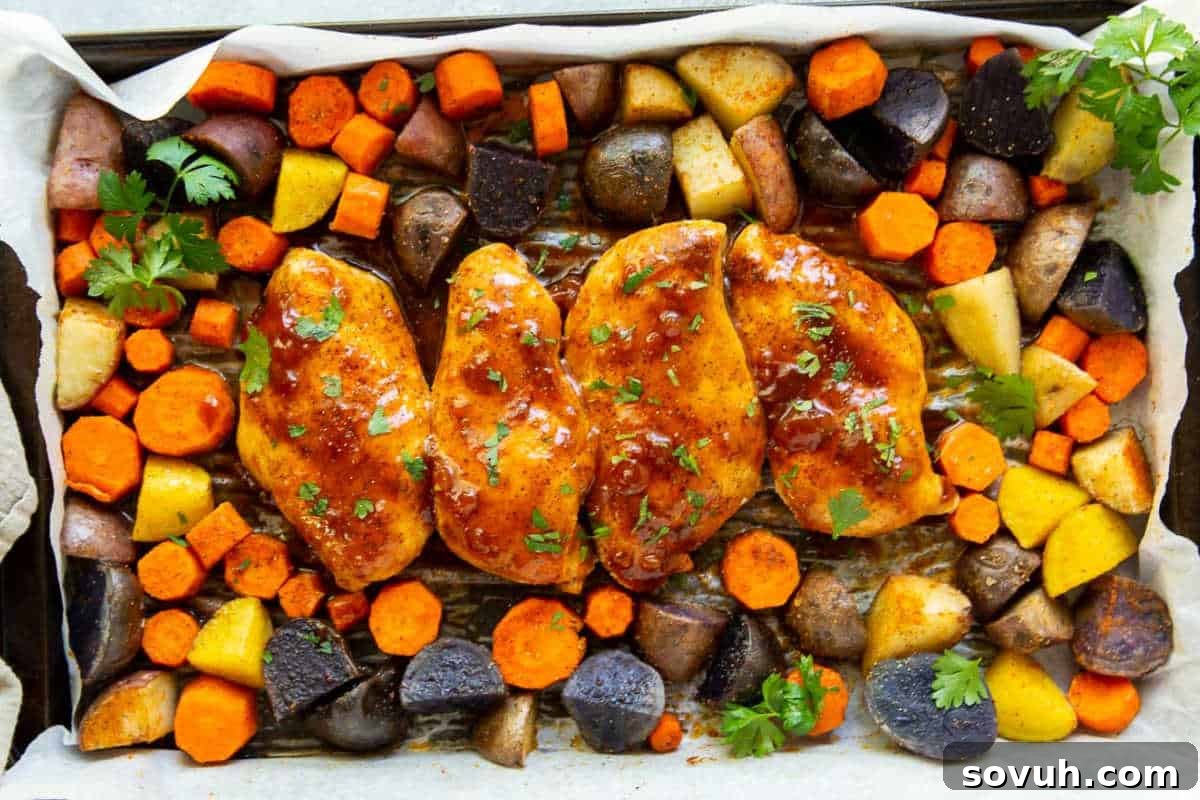 Four seasoned chicken breasts and assorted roasted vegetables, including carrots and potatoes, arranged on a parchment-lined baking sheet.