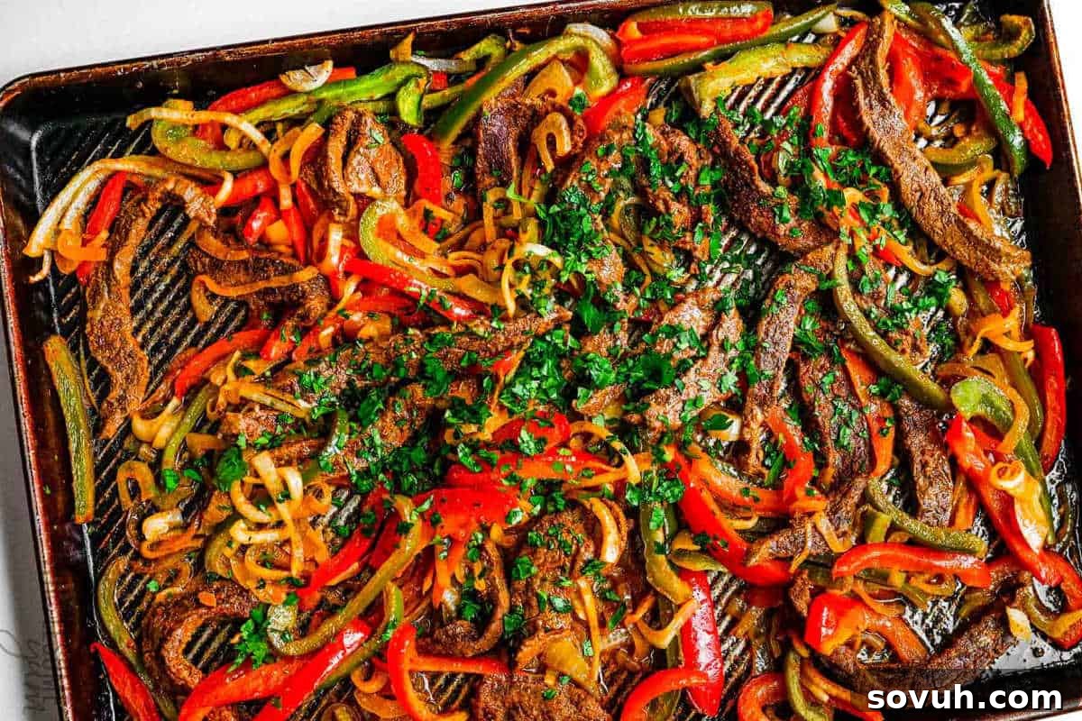 Sheet pan with sliced beef, red and green bell peppers, and onions, garnished with chopped parsley.