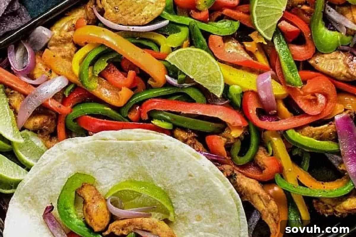 A close-up of chicken fajitas with sliced bell peppers, red onion, and lime wedges, served with a flour tortilla.