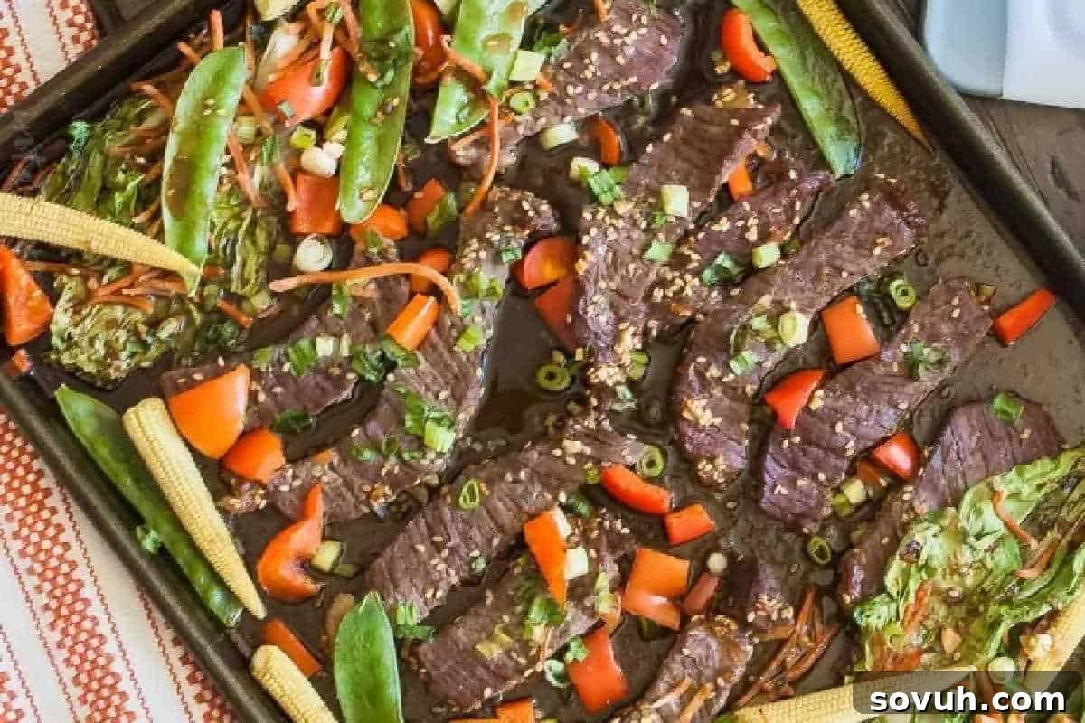 Sheet pan with sliced beef, red bell peppers, baby corn, snap peas, shredded carrots, and chopped scallions, all seasoned and cooked together.