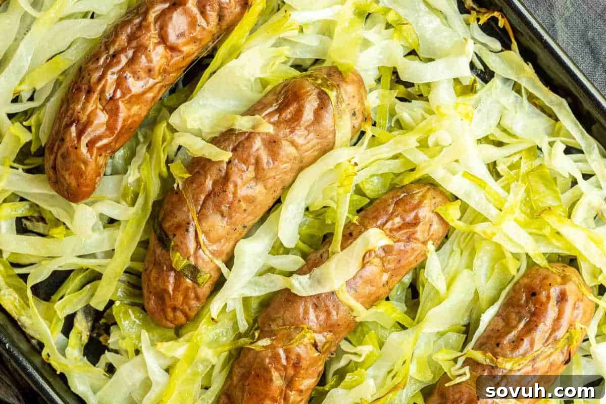 Four cooked sausages laid on a bed of shredded cabbage on a baking tray.