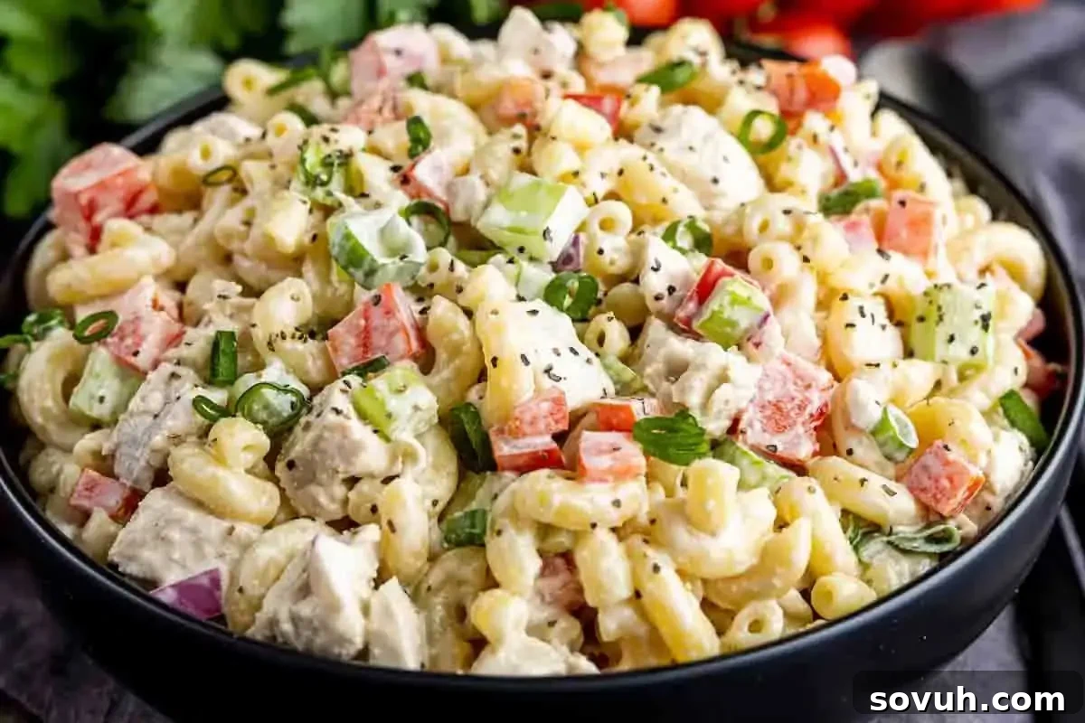 A refreshing Chicken Macaroni Salad in a white bowl, featuring tender macaroni, diced chicken, and colorful vegetables in a creamy dressing, garnished with fresh herbs.
