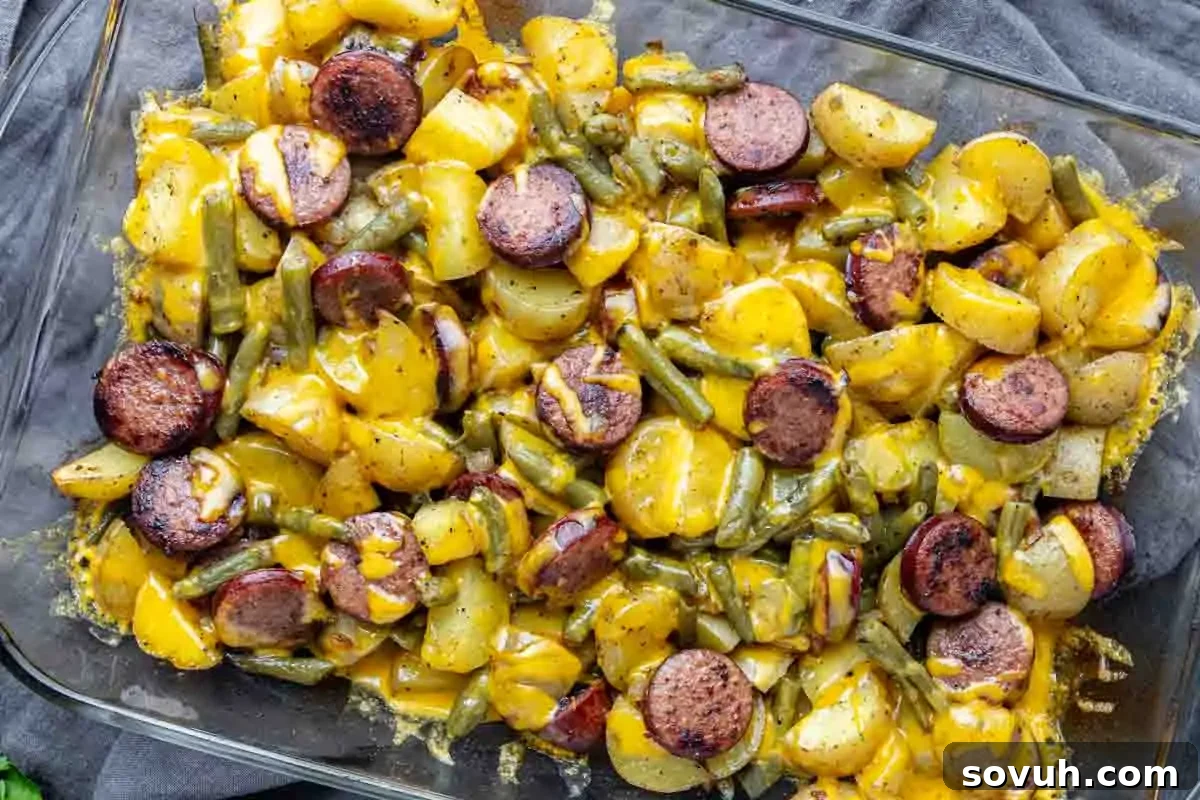 Hearty Sausage, Potato, and Green Bean Bake 2 A glass baking dish filled with sliced potatoes, green beans, sausage rounds, and melted cheddar cheese.