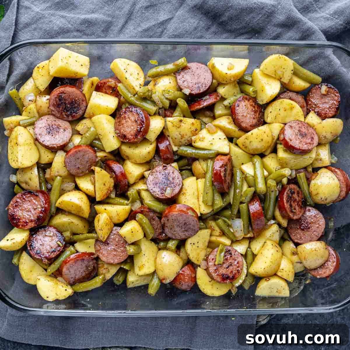 Hearty Sausage, Potato, and Green Bean Bake 4 A glass baking dish filled with sliced sausage, yellow potatoes, and green beans, all seasoned and roasted.