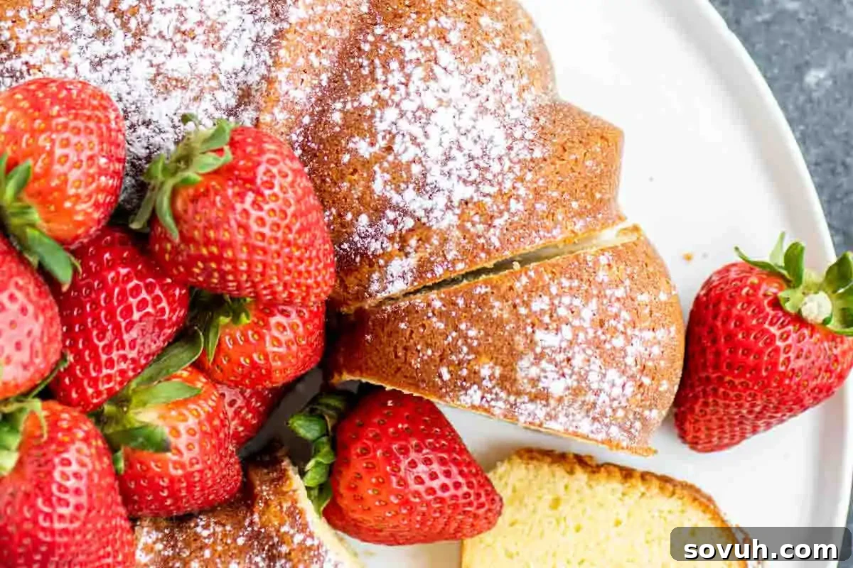 A close-up of a sliced cake dusted with powdered sugar, accompanied by fresh strawberries on a white plate.