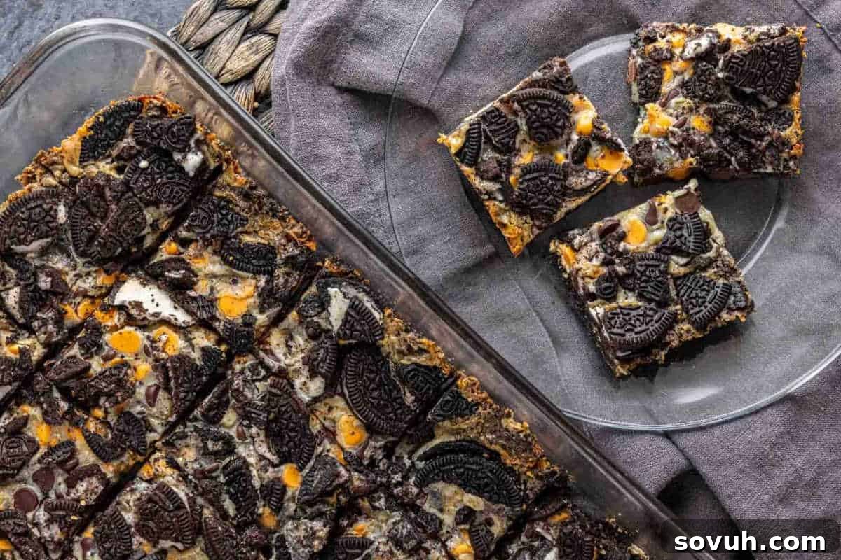 Glass baking dish filled with chocolate and cookie bar squares, with two squares served on a small glass plate, placed on a gray cloth.