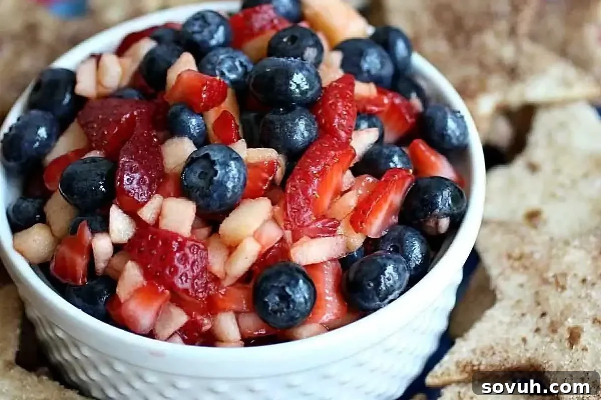 A white bowl filled with a fruit salad containing blueberries, diced strawberries, and apple pieces, surrounded by star-shaped crackers.