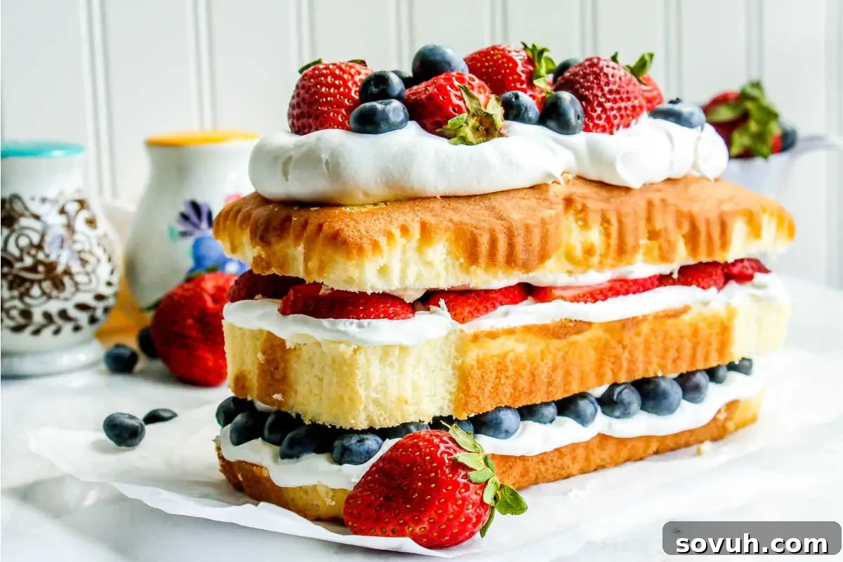 A layered sponge cake with whipped cream, strawberries, and blueberries on a white surface.