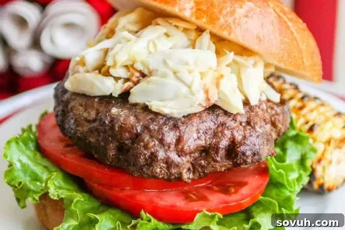 A hamburger with a beef patty, shredded cabbage, tomato slices, and lettuce on a bun, served on a white plate.