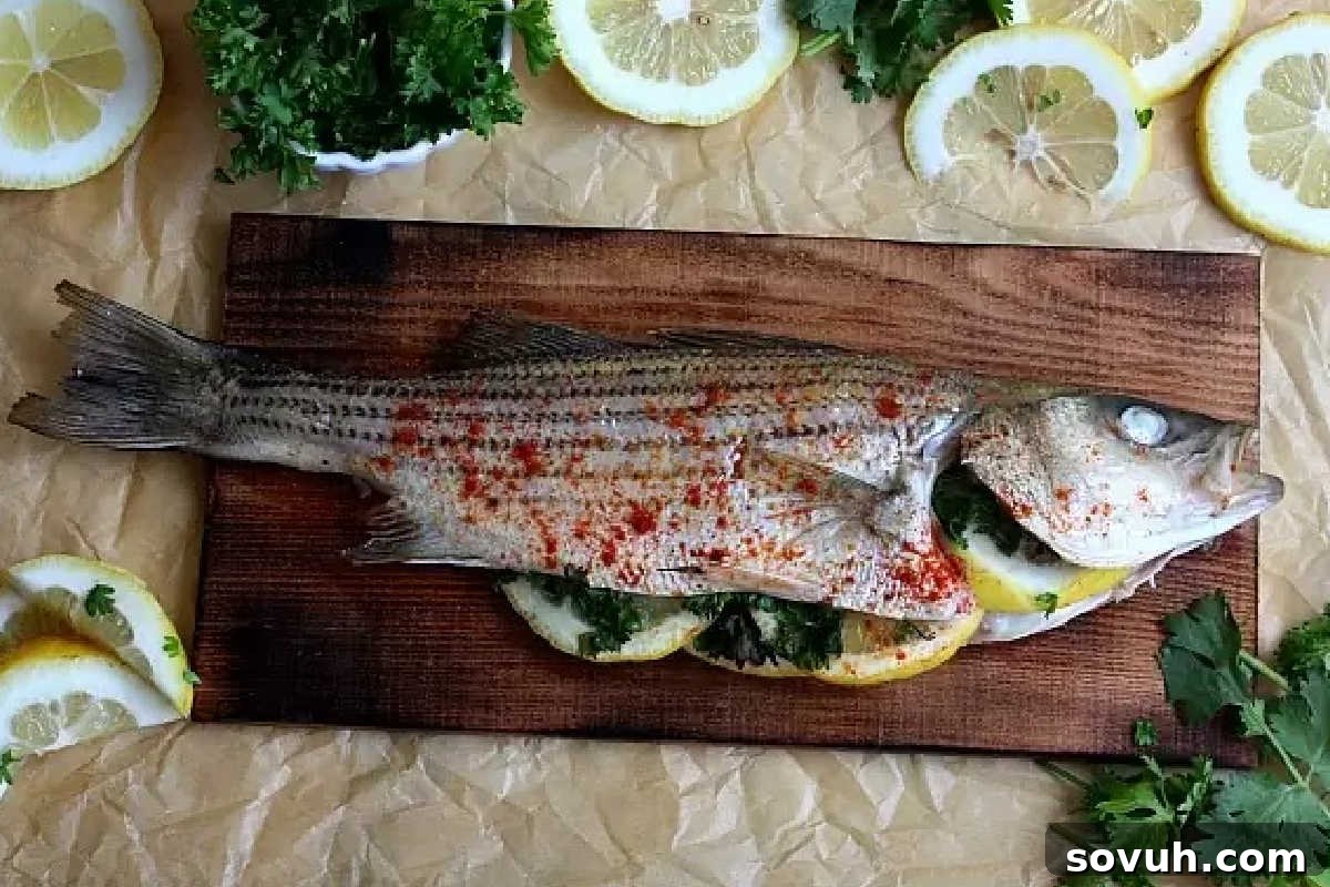 A whole cooked fish garnished with lemon slices and herbs is placed on a wooden board, surrounded by additional lemon slices and fresh parsley.