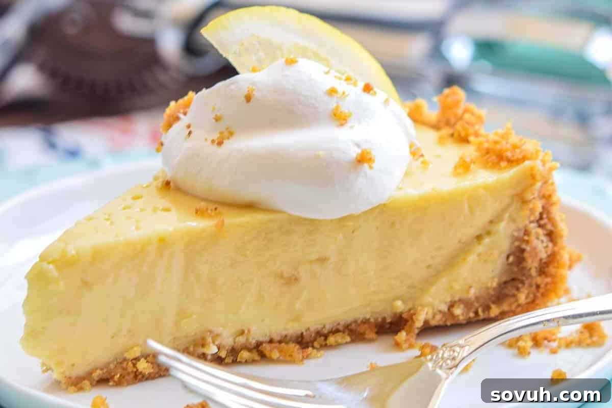 A slice of lemon pie with a crumbly crust, topped with whipped cream and a lemon slice, on a white plate with a fork.