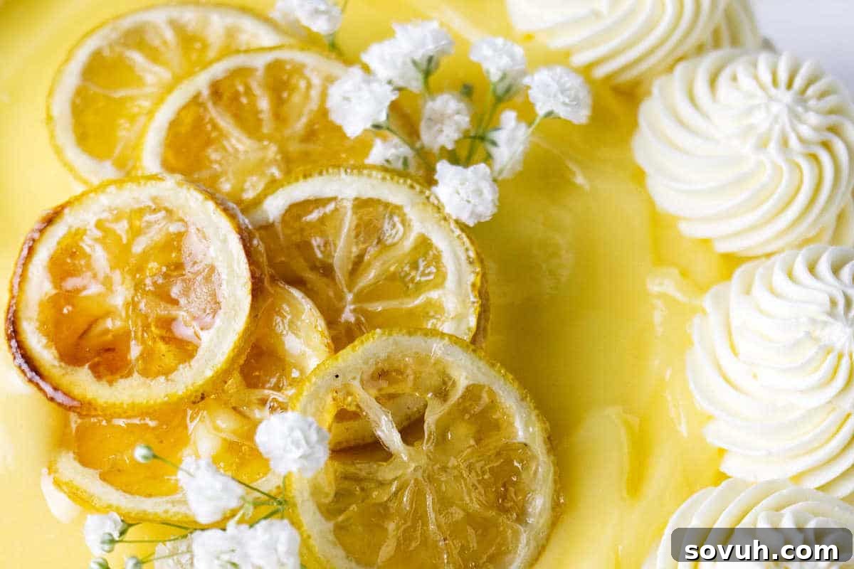 Close-up of a lemon cake topped with lemon slices, white whipped cream swirls, and small white flowers.