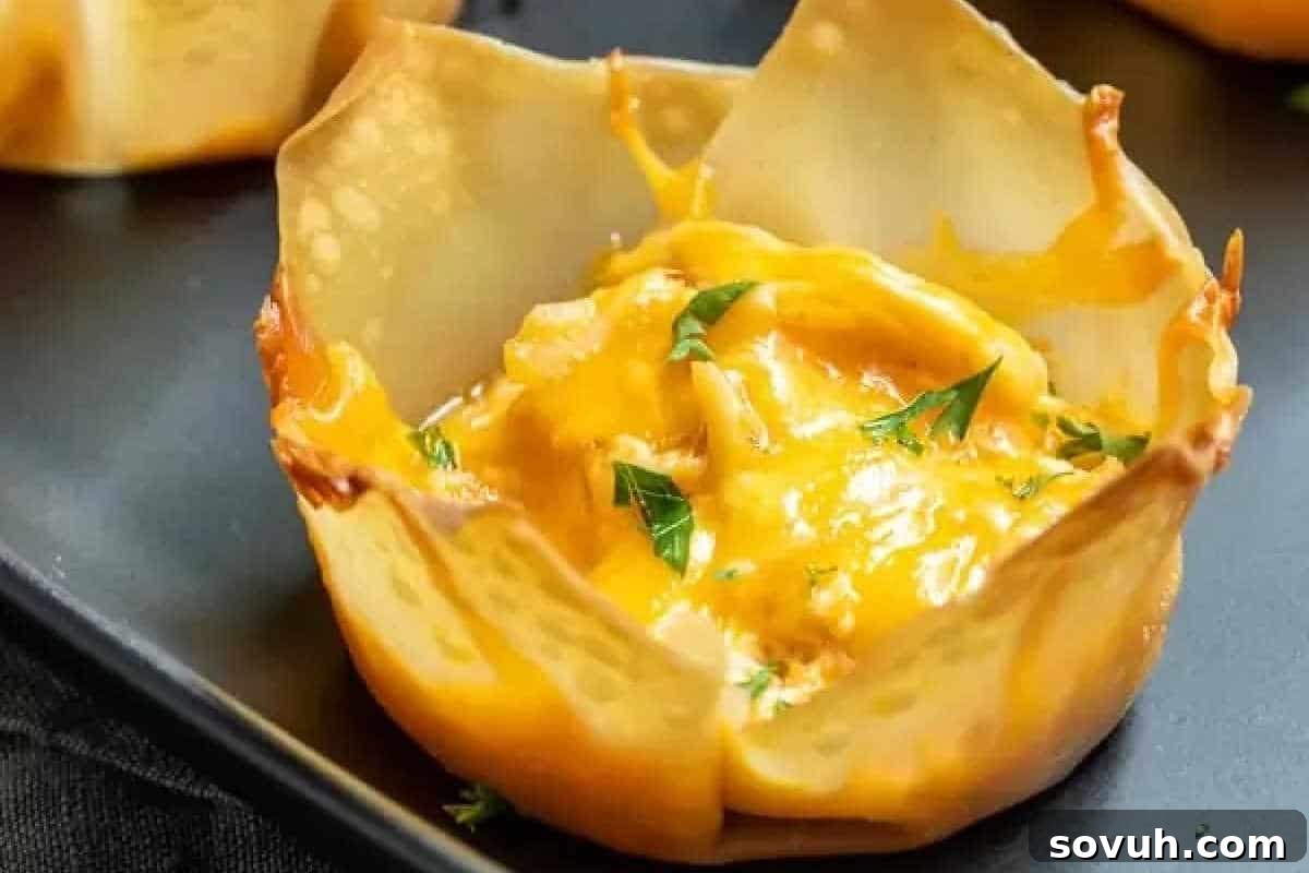 A baked wonton cup filled with melted cheese and garnished with chopped herbs on a dark tray.