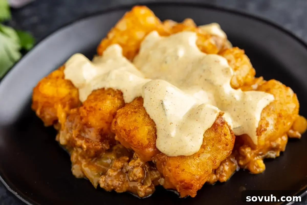 A delicious plate of tater tot casserole, generously topped with a creamy special sauce, showcasing golden brown tater tots and the savory ground meat mixture peeking out from beneath.