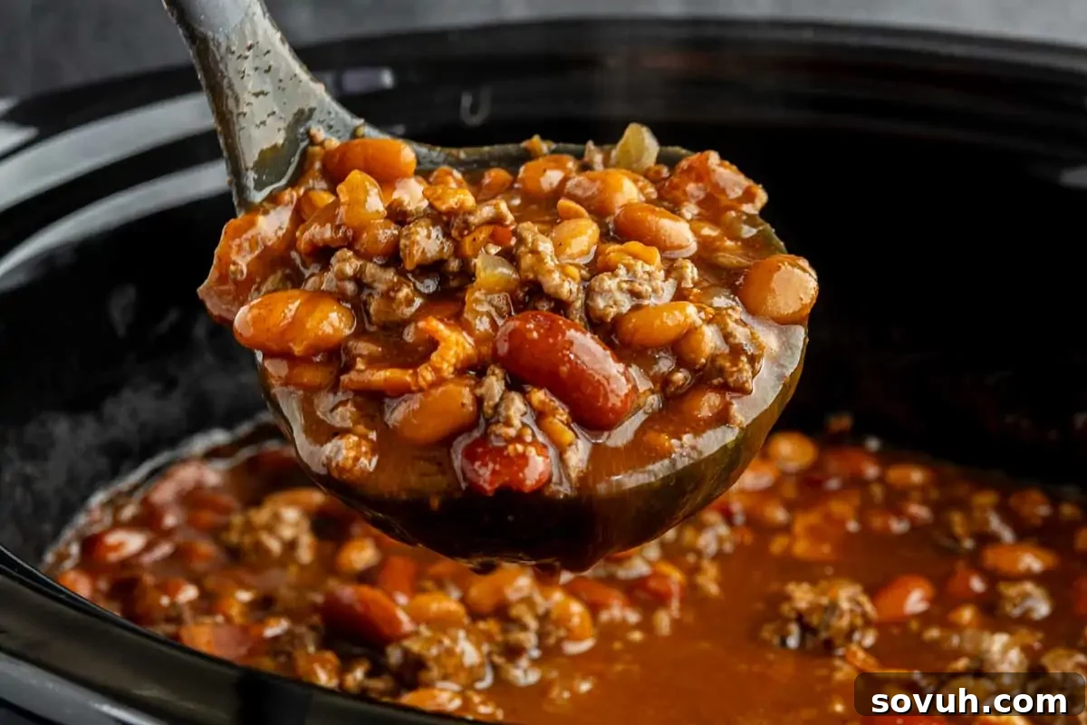 A large ladle lifting a generous serving of hearty chili, rich with beans and ground meat, from a black slow cooker, promising a comforting meal.