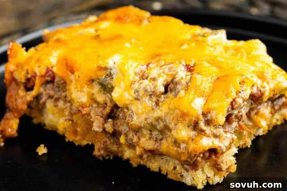 A captivating close-up of a perfectly sliced piece of John Wayne Casserole, showcasing its golden melted cheese topping and distinct layers including seasoned ground beef, vibrant vegetables, and a comforting biscuit base.