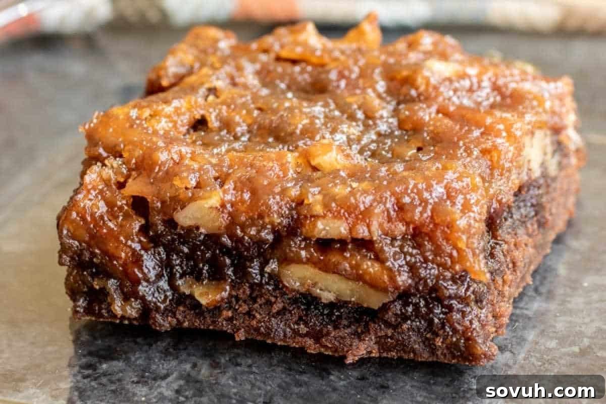 A detailed close-up of a single pecan pie brownie, showcasing its rich, gooey, caramelized pecan topping beautifully contrasting with a dense, dark chocolate brownie base.