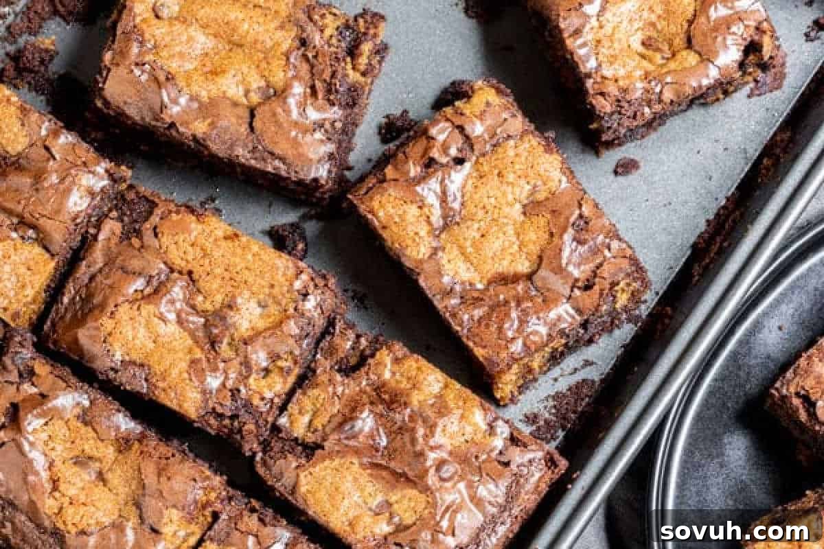 A baking tray filled with freshly baked, perfectly sliced brookies, showcasing a beautiful marbled top of rich chocolate brownie and classic chocolate chip cookie dough.