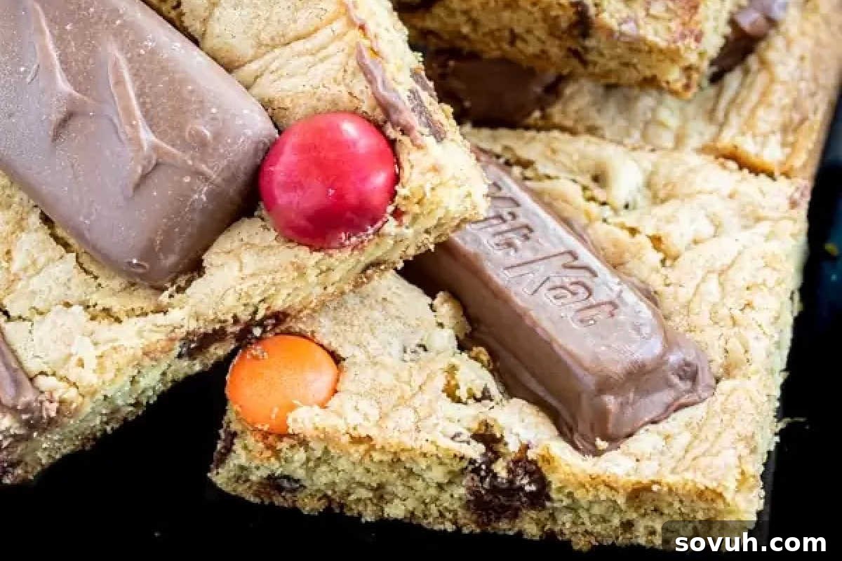 A tempting close-up of dessert bars generously studded with various embedded chocolate pieces and vibrantly colorful candy-coated chocolates on top.