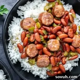 A black bowl filled with white rice, red kidney beans, sliced sausage, and chopped green bell peppers.