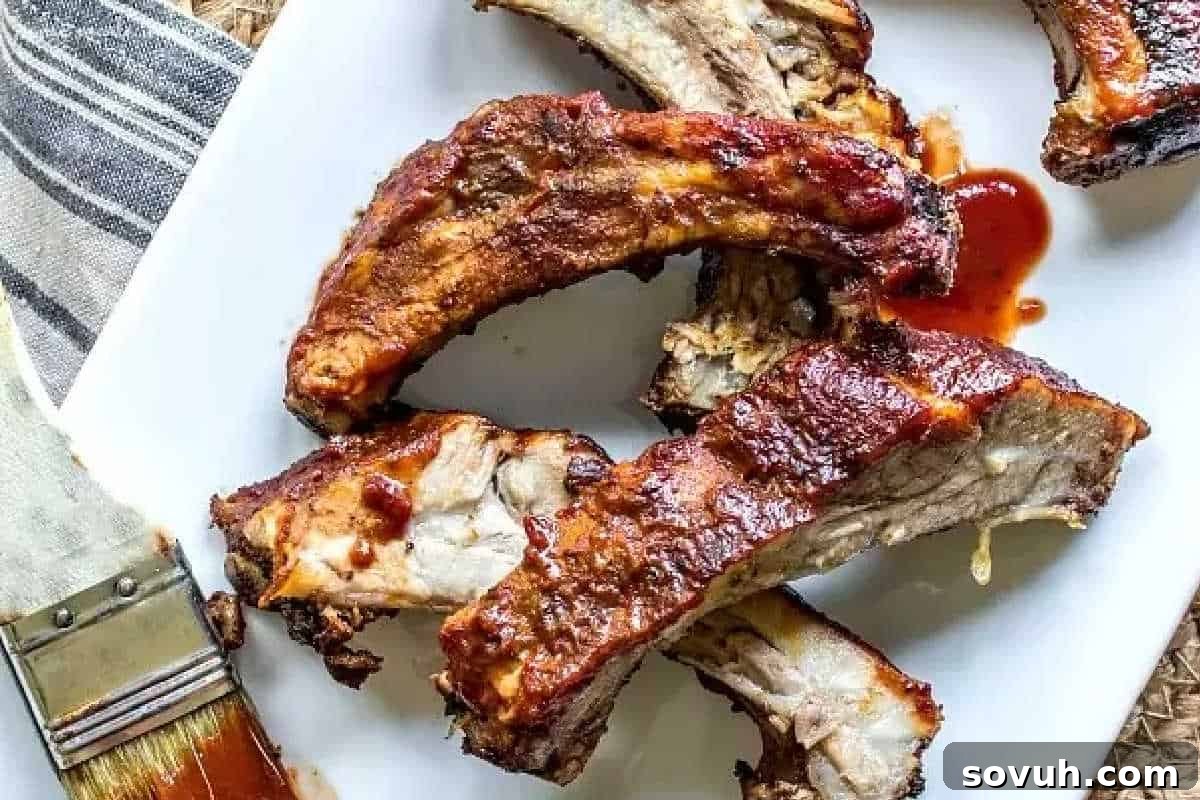 A pristine white plate showcases several perfectly cooked barbecue ribs, glistening with sweet BBQ sauce. A basting brush with sauce residue rests alongside, positioned on a rustic cloth napkin, highlighting the delicious preparation of these tender ribs.