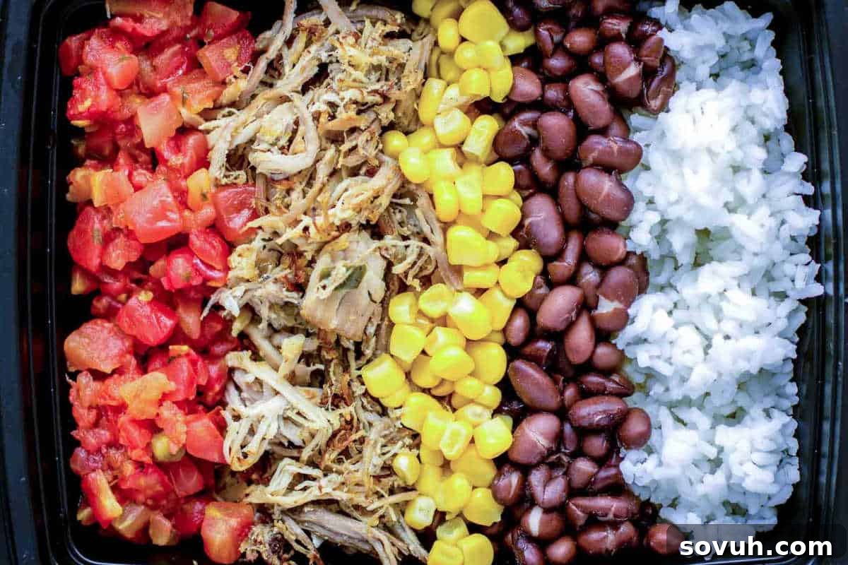 A rectangular container bursting with colorful layers of delicious ingredients, featuring diced tomatoes, perfectly shredded meat, golden corn kernels, rich black beans, and fluffy white rice, creating a vibrant and satisfying meal.
