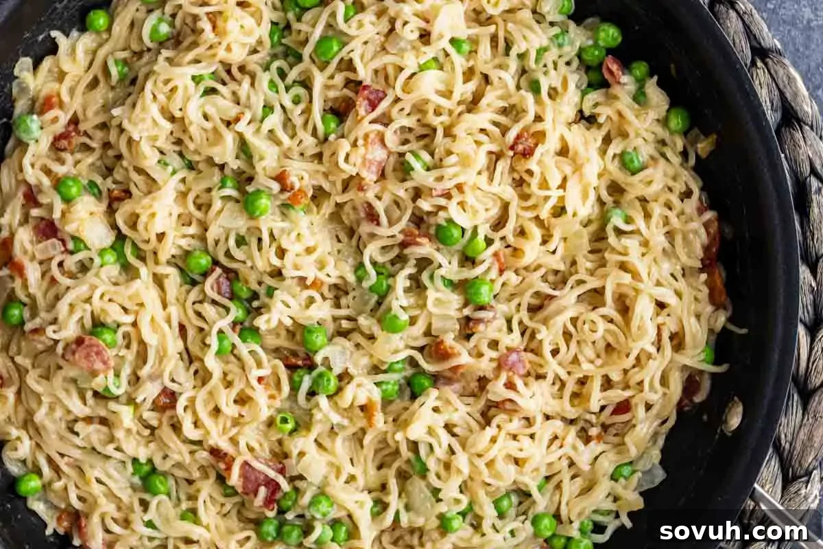Effortless Ramen Carbonara 2 A skillet filled with bacon ramen carbonara—cooked ramen noodles, green peas, bacon pieces, and a creamy sauce for an easy homemade twist.