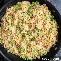 Effortless Ramen Carbonara 6 A skillet filled with homemade ramen carbonara—cooked ramen noodles mixed with green peas and small pieces of bacon in a creamy sauce.