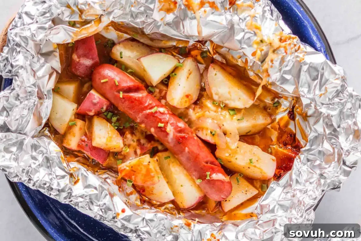 A foil packet containing cooked sausage, potato wedges, and vegetables, garnished with herbs, placed on a blue plate.