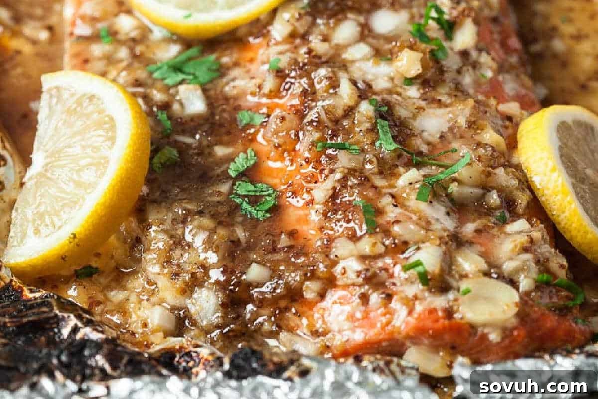 Close-up of a baked salmon fillet seasoned with chopped onions, garlic, herbs, and lemon slices, shown in a foil-lined pan.