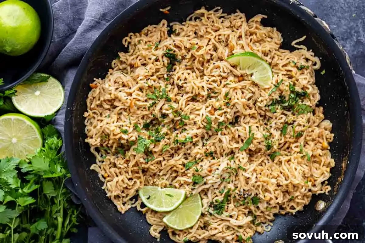 A skillet filled with cooked peanut butter ramen noodles garnished with chopped herbs and lime wedges, with fresh limes and cilantro nearby—an easy ramen recipe perfect for quick meals.