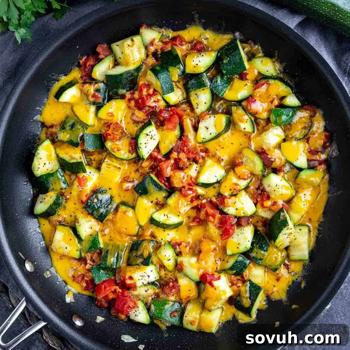 Sautéed zucchini and tomatoes with melted cheddar cheese in a black summer zucchini skillet, garnished with black pepper.