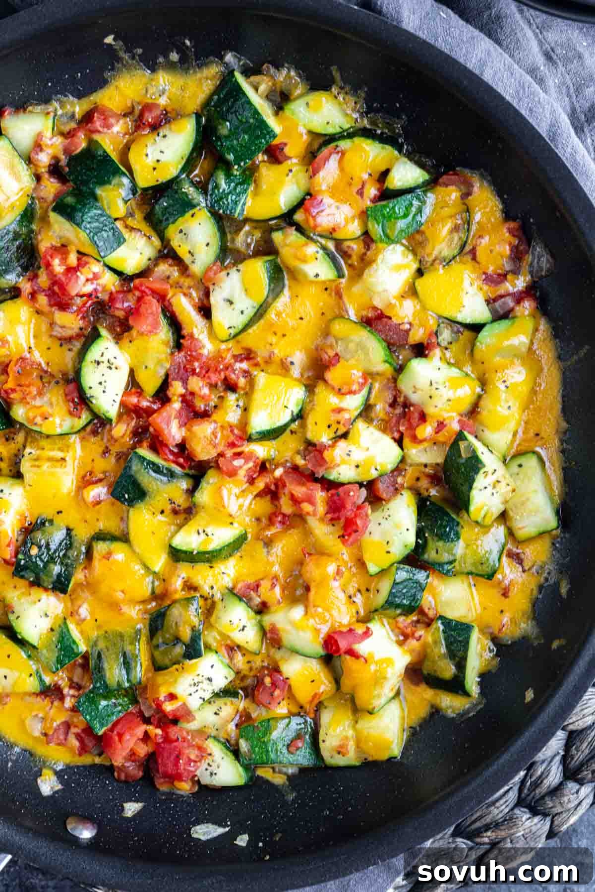 A cheesy zucchini skillet featuring chopped zucchini, melted cheddar cheese, diced tomatoes, and onions, seasoned with black pepper—a perfect summer zucchini skillet for easy sautéed dinners.