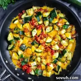 Sautéed zucchini and tomatoes with melted cheddar cheese in a black summer zucchini skillet, garnished with black pepper.