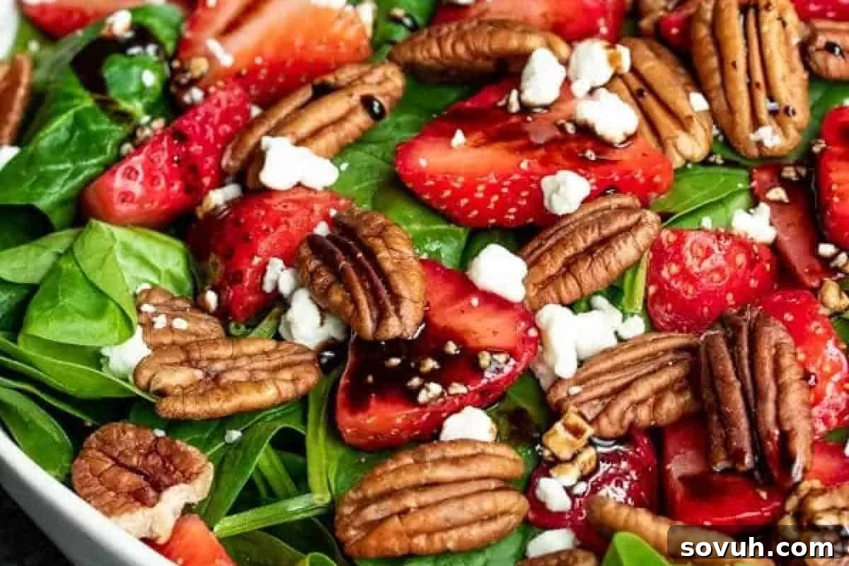 A wholesome spinach salad generously topped with thinly sliced vibrant strawberries, whole toasted pecans, crumbled feta cheese, and a light drizzle of balsamic dressing, creating a refreshing and visually appealing dish.