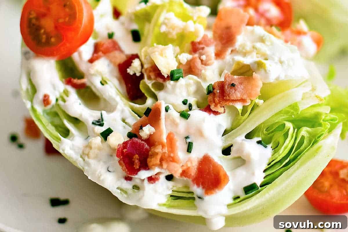 A close-up of a classic Wedge Salad, showcasing a crisp iceberg lettuce wedge generously topped with a creamy blue cheese dressing, savory bacon bits, fresh chopped chives, diced tomatoes, and rich crumbled blue cheese, artfully presented on a clean white plate.