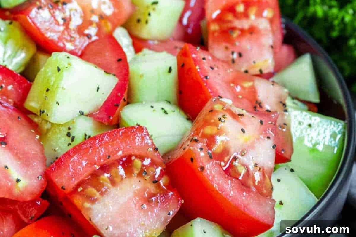 A vibrant close-up of a refreshing salad, showcasing perfectly chopped red tomatoes and crisp green cucumbers, lightly seasoned with freshly ground black pepper and aromatic herbs, creating a simple yet delicious side dish.