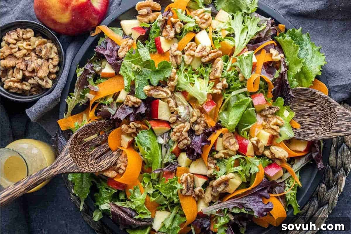 A vibrant bowl of mixed green salad overflowing with crunchy walnuts, delicate slices of fresh peaches, crisp apple pieces, and artistic carrot ribbons, elegantly presented with wooden salad servers resting beside and a small bowl of walnuts nearby, ready to be enjoyed.