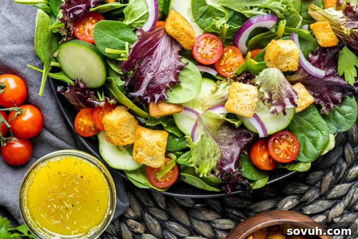 A generously filled bowl of vibrant mixed green salad, featuring ruby-red cherry tomatoes, cool cucumber slices, thinly sliced red onion, and crunchy golden croutons, elegantly served with a small side bowl of tangy vinaigrette dressing, perfect for a refreshing meal.