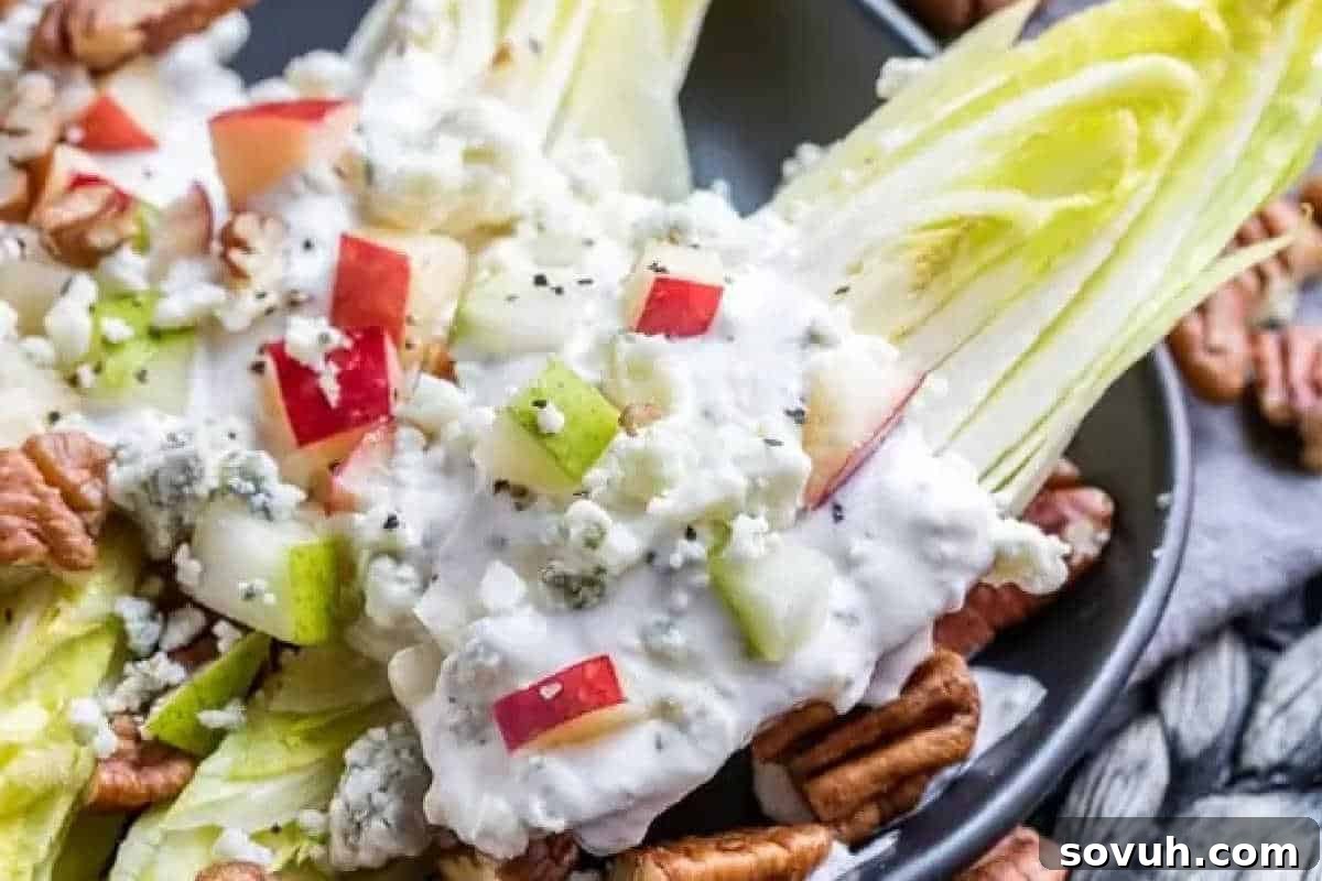 An elegant plate showcases a wedge salad, generously topped with a rich blue cheese dressing, crisp chopped apples, sweet diced pears, crumbled blue cheese, and toasted pecans, creating a sophisticated blend of flavors and textures.