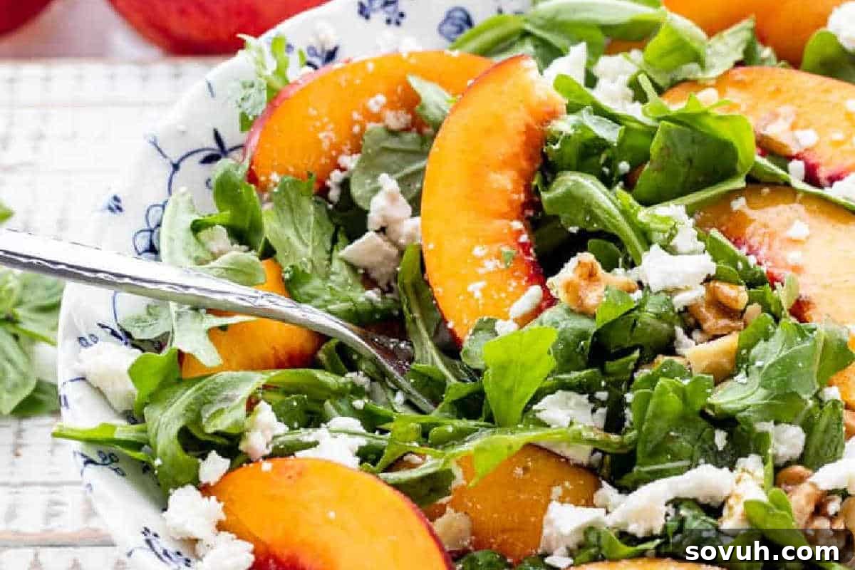 A refreshing bowl of salad featuring vibrant green arugula, sweet and juicy peach slices, crumbled feta cheese, and crunchy walnuts, with a fork partially visible, inviting a taste of this delightful combination.
