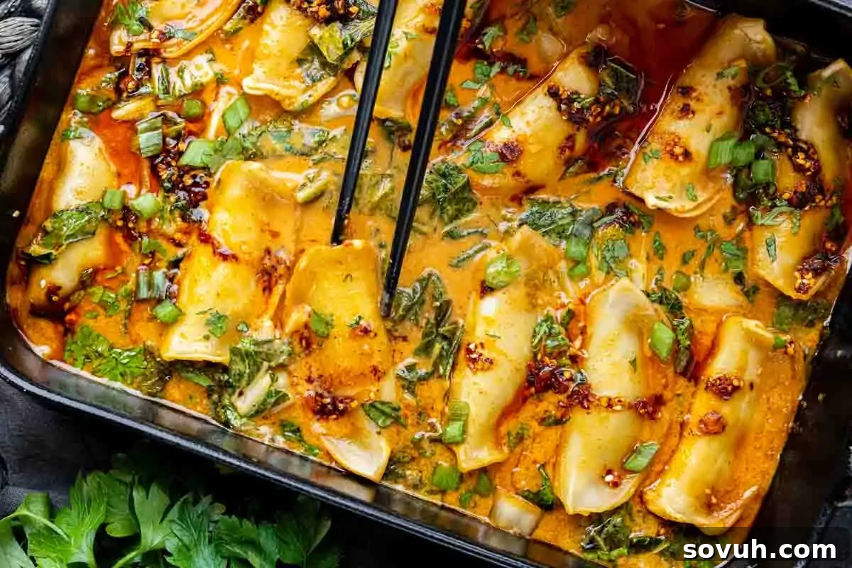 Close-up of dumplings in a spicy broth with greens, inspired by a viral TikTok dumpling recipe; garnished with chopped scallions and cilantro, as chopsticks hold one dumpling above the dish.