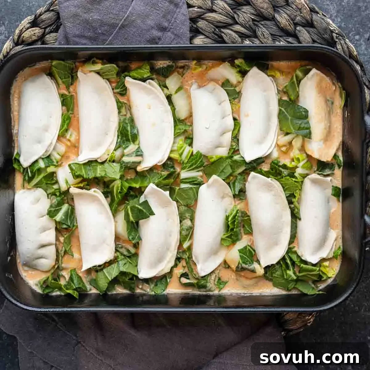 A baking dish filled with uncooked dumplings arranged over chopped greens and sauce, inspired by the viral TikTok dumpling recipe, ready to be baked.