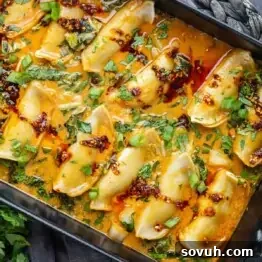 A tray of dumplings in a spicy orange sauce, garnished with chopped green onions and herbs.