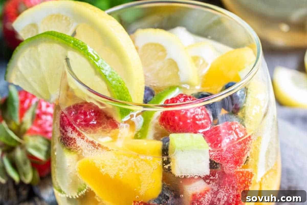 A glass of sparkling fruit punch with slices of lemon and lime, and assorted berries and fruit pieces.