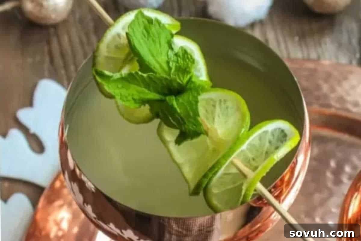 A copper mug filled with a light-colored drink, garnished with fresh mint leaves and lime slices on a skewer.