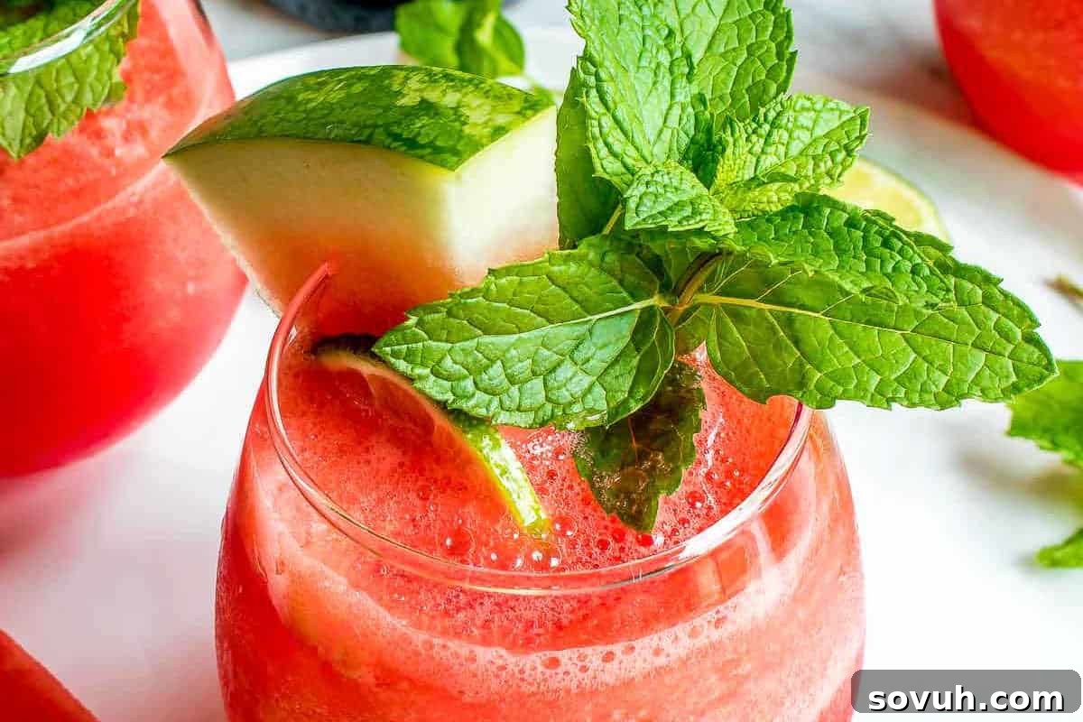 A glass of watermelon drink garnished with a watermelon slice, lime wedge, and fresh mint leaves.