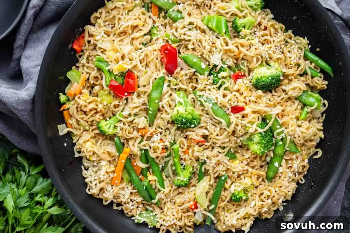 A skillet filled with vibrant ramen vegetable stir fry, showcasing cooked noodles mixed with broccoli, green beans, colorful bell peppers, and onions, all generously topped with toasted sesame seeds.
