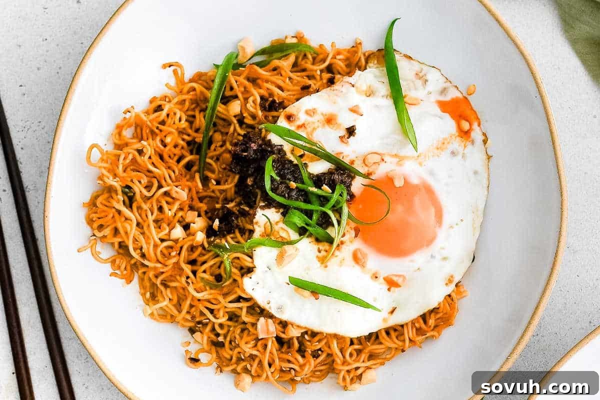 A plate of expertly stir-fried noodles, crowned with a perfectly cooked sunny-side-up egg, a sprinkle of chopped peanuts, a drizzle of dark, rich sauce, and a generous garnish of sliced green onions.