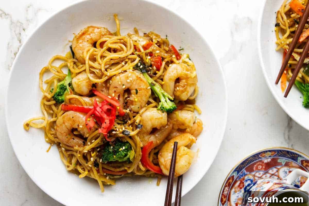 A vibrant plate of shrimp stir-fried noodles, featuring crisp broccoli, bright red bell peppers, delicate pickled ginger, and a sprinkle of sesame seeds, elegantly served with chopsticks.